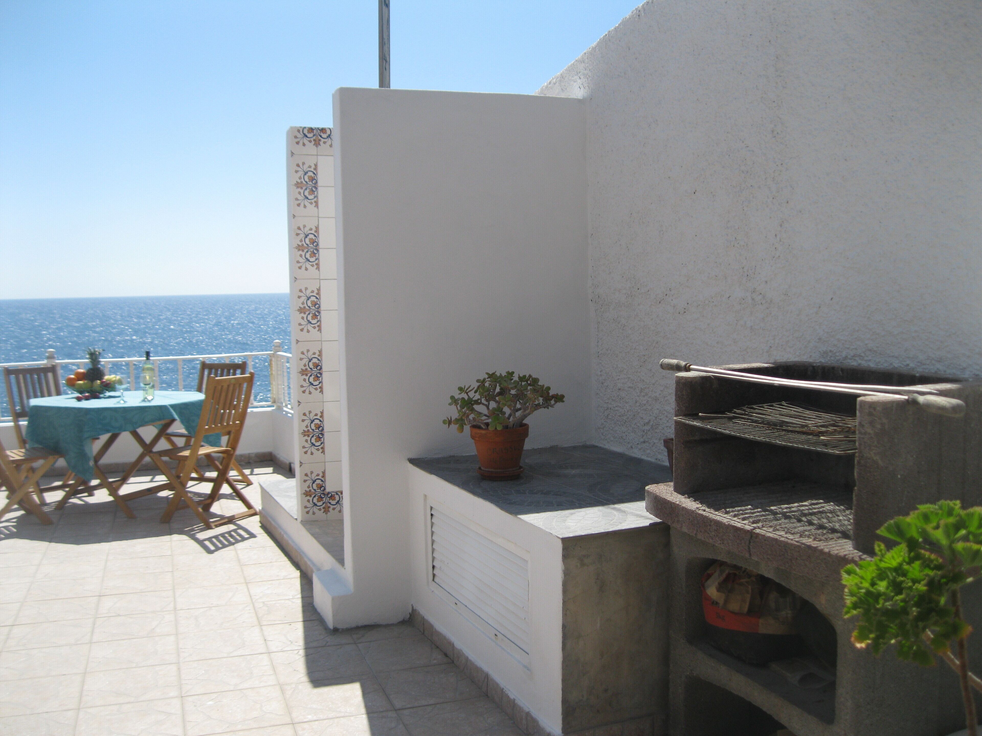 En terrasse med et bord dækket til to personer, en potteplante og en grill.