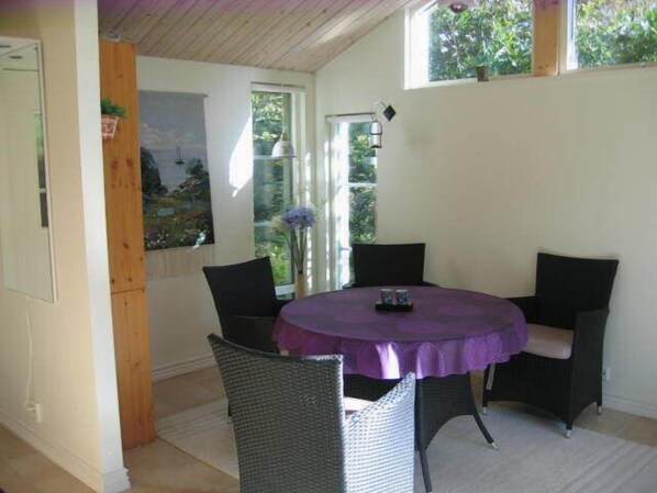 A room with a round table, four chairs, a purple tablecloth, and a window with a view of greenery.