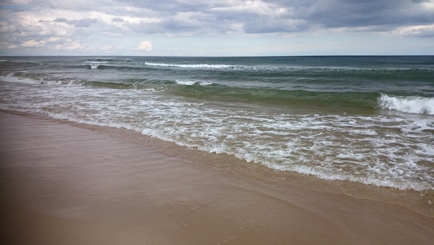 Een strand met golven die zachtjes op de kust komen, onder een bewolkte lucht.