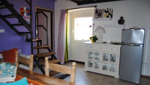 Une cuisine équipée d’un réfrigérateur, d’une fenêtre avec des rideaux, d’un meuble avec des portes en verre et d’une table en bois.