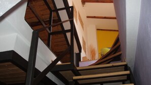 Un escalier en bois doté d’une structure en métal noir, menant à une pièce dont un mur est jaune et qui possède une fenêtre.
