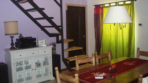 Un coin repas avec une table en bois, des chaises, un chemin de table rouge, un buffet blanc aux portes vitrées, une lampe et un escalier.