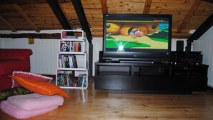 Un salon avec un téléviseur diffusant un match, une bibliothèque remplie de livres, un canapé rouge et un plafond en bois.