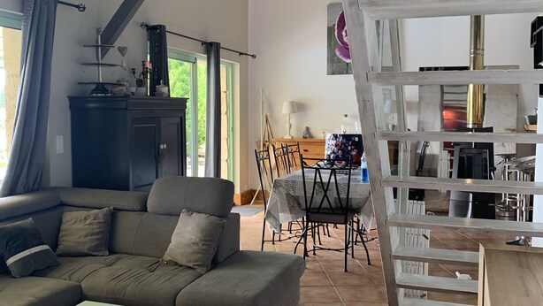 A spacious living area with a large sofa, a dining table, and a kitchen area with a staircase. - House / Villa - Sainte sabine (Beaumontois En Périgord)