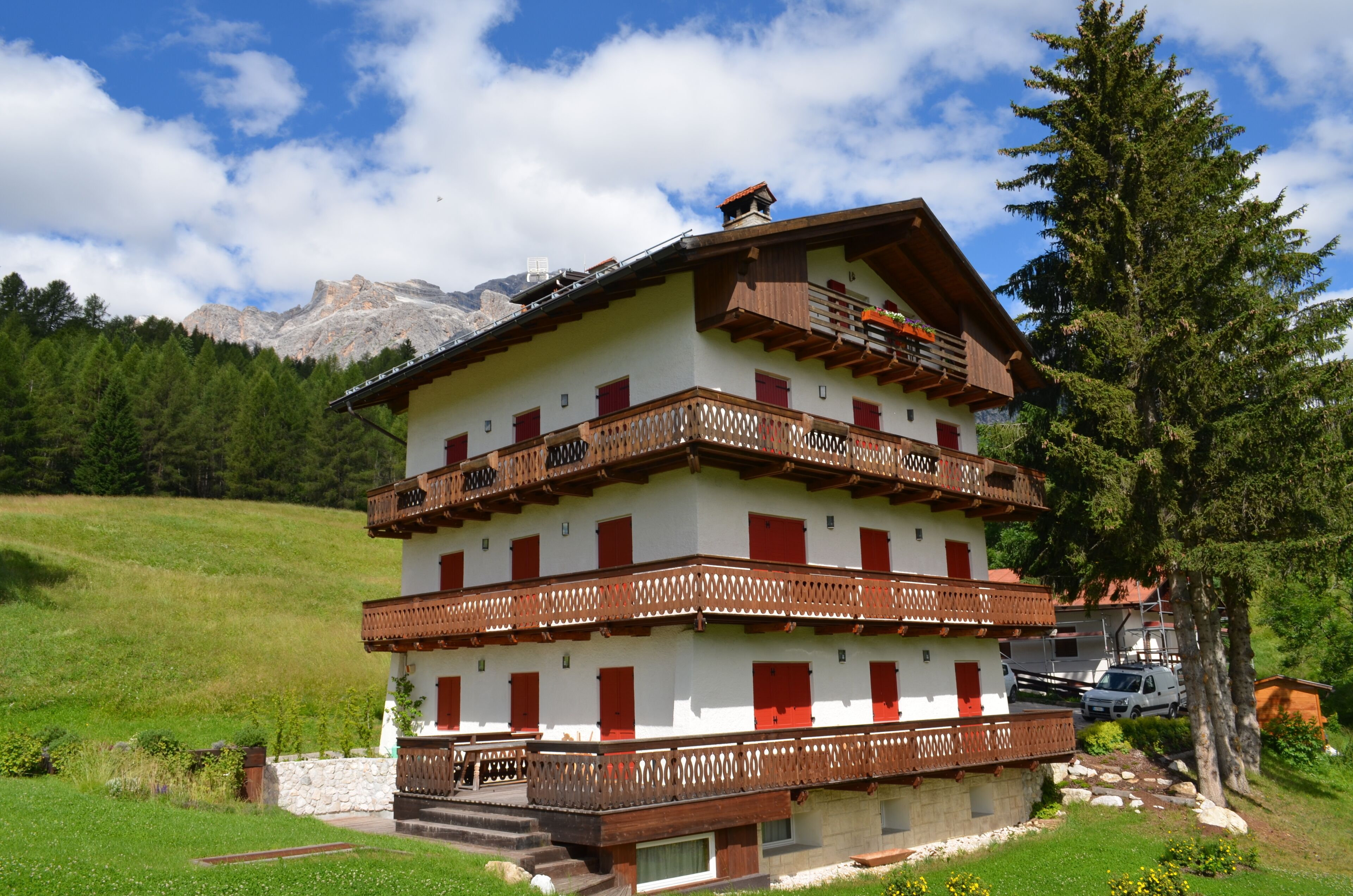 A multi-story chalet with balconies, set in a mountainous area with a clear sky.
