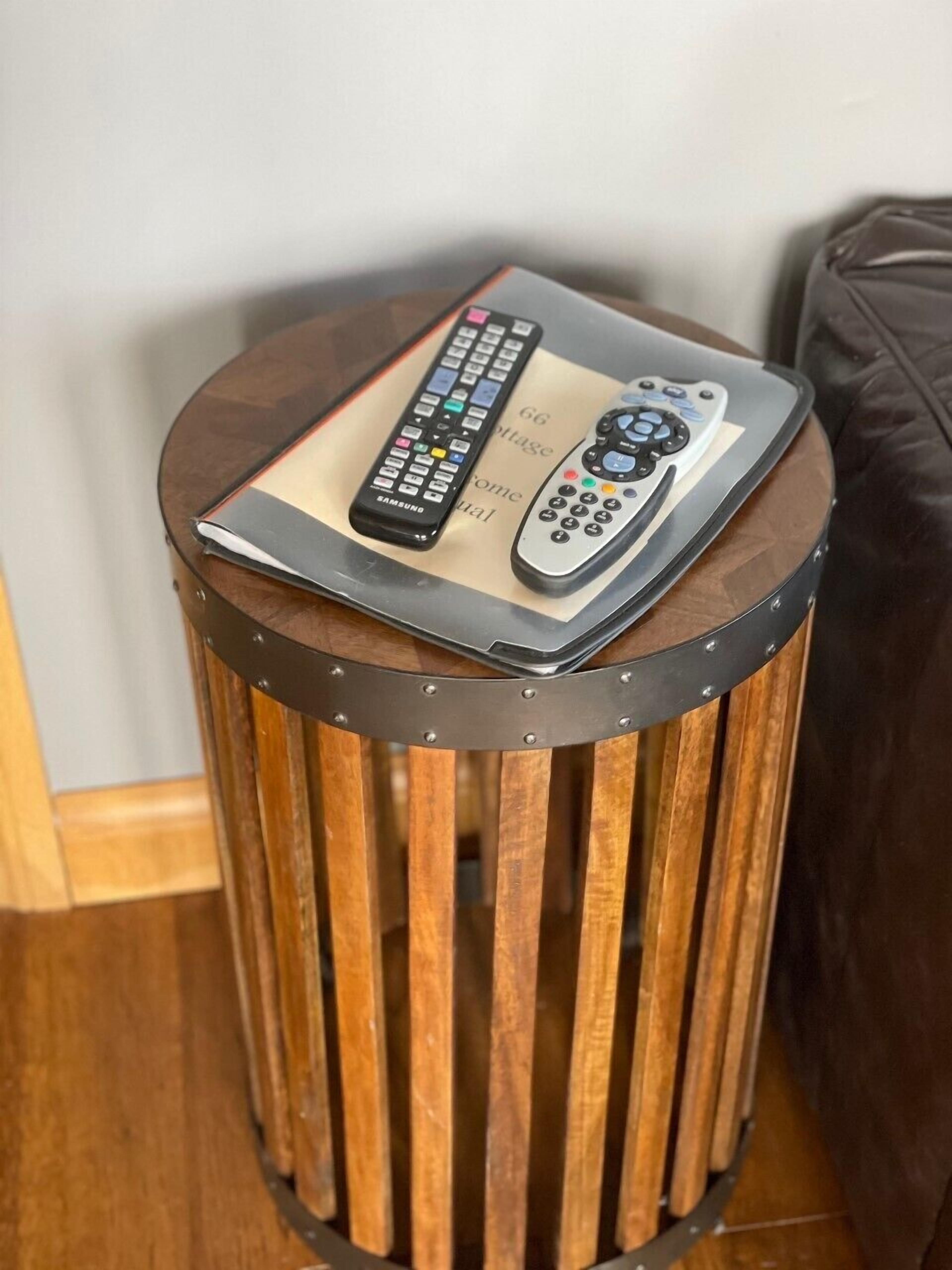A round wooden side table with two remote controls on top.