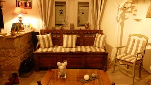 Ein gemütliches Wohnzimmer mit einem Holzsofa, gestreifteren Kissen, einem Couchtisch mit Dekoration und einem Sessel sowie einer Lampe.
