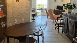 Uma área de refeições com uma mesa e cadeiras de madeira, um sofá, uma televisão e um vaso de planta.