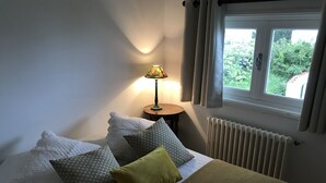Quarto com cama, almofadas, abajur, janela e radiador.