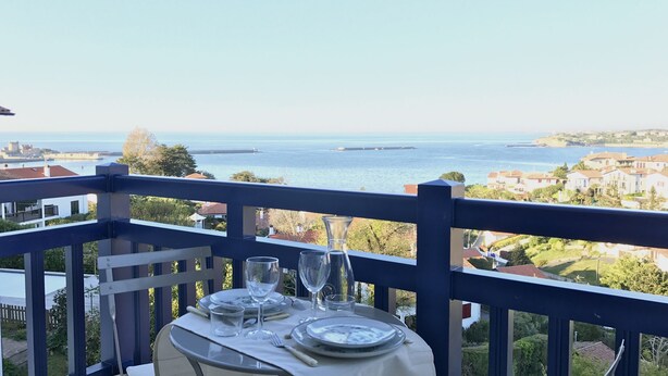 Mesa posta para dois, com vista para o mar e área residencial ao fundo.