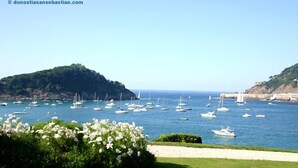 Un paysage côtier avec des bateaux sur l’eau, une zone herbeuse au premier plan et des collines en arrière-plan.