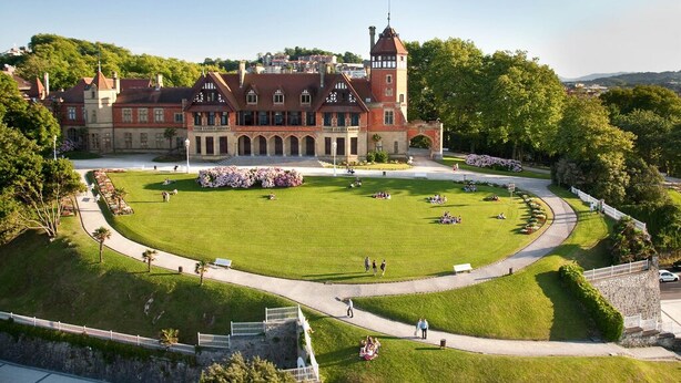 Un grand bâtiment historique doté d’une cour intérieure, entouré d’une végétation luxuriante et bordé d’une allée pavée.