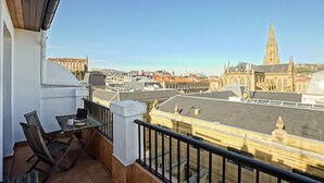 Un balcon avec une table et des chaises, donnant sur un paysage urbain avec des bâtiments historiques et une tour imposante.