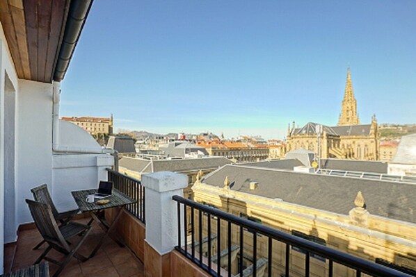 A balcony with a table and chairs, overlooking a cityscape with historic buildings and a prominent tower.