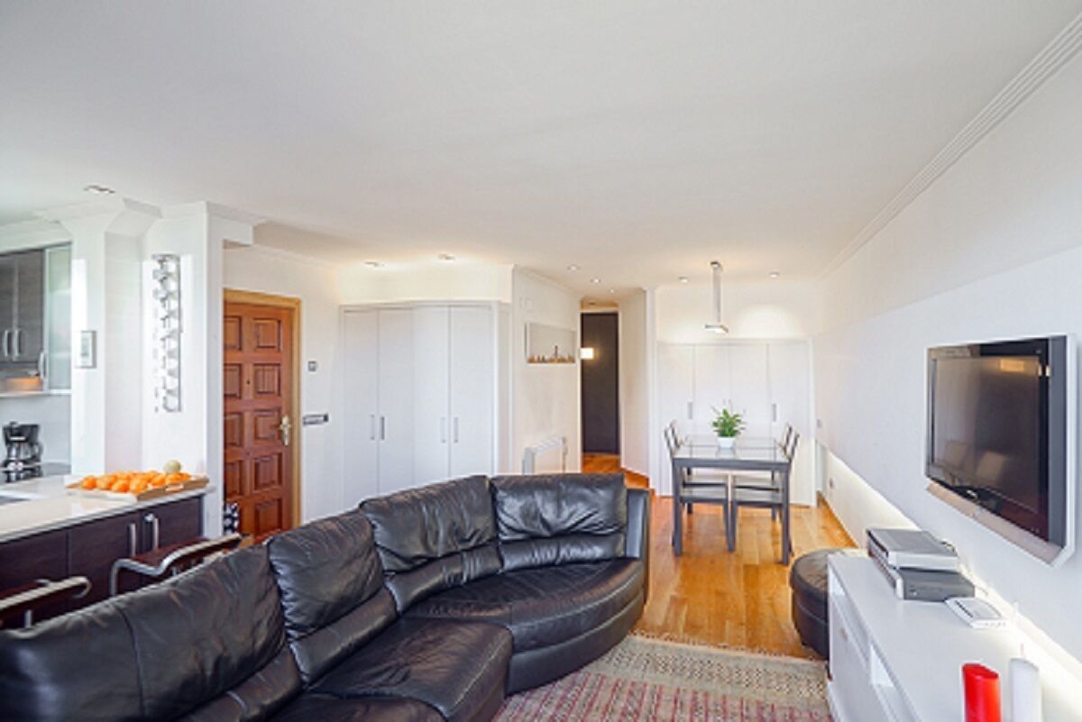 Een moderne woonkamer met een zwarte leren bank, een eethoek met een tafel en stoelen, en een keuken met kasten en een aanrecht.