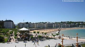 Un paseo marítimo con playa, un quiosco y una hilera de edificios al fondo.