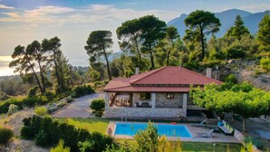 Une maison en pierre avec un toit de tuiles rouges, une piscine et une vue sur la mer et les montagnes.
