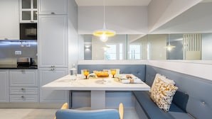 A modern kitchen with a built-in seating area, a dining table set with orange drinks, and a large window providing natural light. - Victoria Project - Apartment I - Private Parking (Porto)