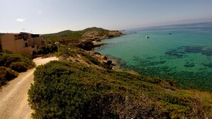 A coastal landscape with a dirt path, buildings, and clear blue sea. - Exclusive penthouse overlooking the sea ....... with deserted beach under the house. (Alghero)