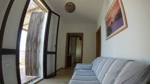 A room with a sofa, a door with a curtain, a hanging light fixture, and a framed picture on the wall. - Exclusive penthouse overlooking the sea ....... with deserted beach under the house. (Alghero)