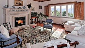Un salon chaleureux avec une cheminée, des fauteuils confortables et une grande fenêtre donnant sur l’extérieur.