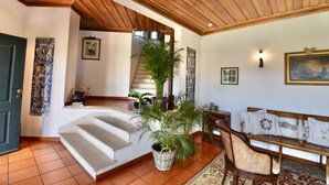 Un escalier menant à un deuxième étage, un banc en bois, un panier en osier rempli de plantes et un tapis à motifs.