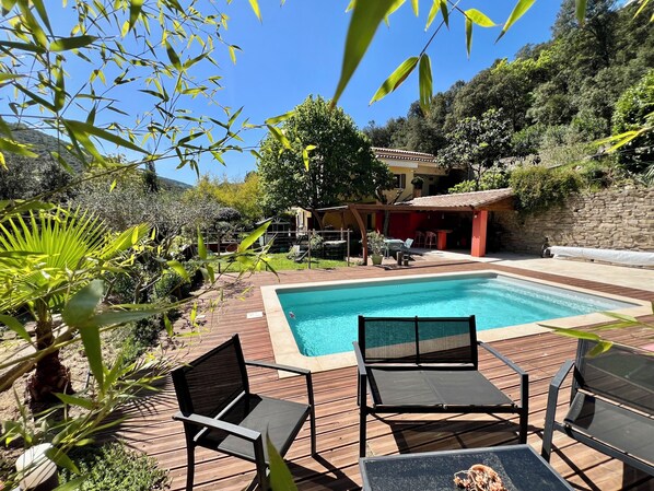 A swimming pool with a wooden deck, outdoor seating, and a stone wall.