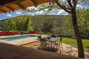 A wooden deck with a pool, outdoor furniture, and a view of a forested hillside.