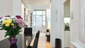 Una cocina moderna con una tetera sobre la encimera, un comedor con un jarrón de flores y un pasillo que conduce a un dormitorio.