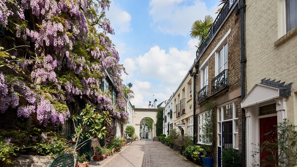 Una estrecha calle adoquinada flanqueada por edificios, algunos con balcones y macetas de flores.