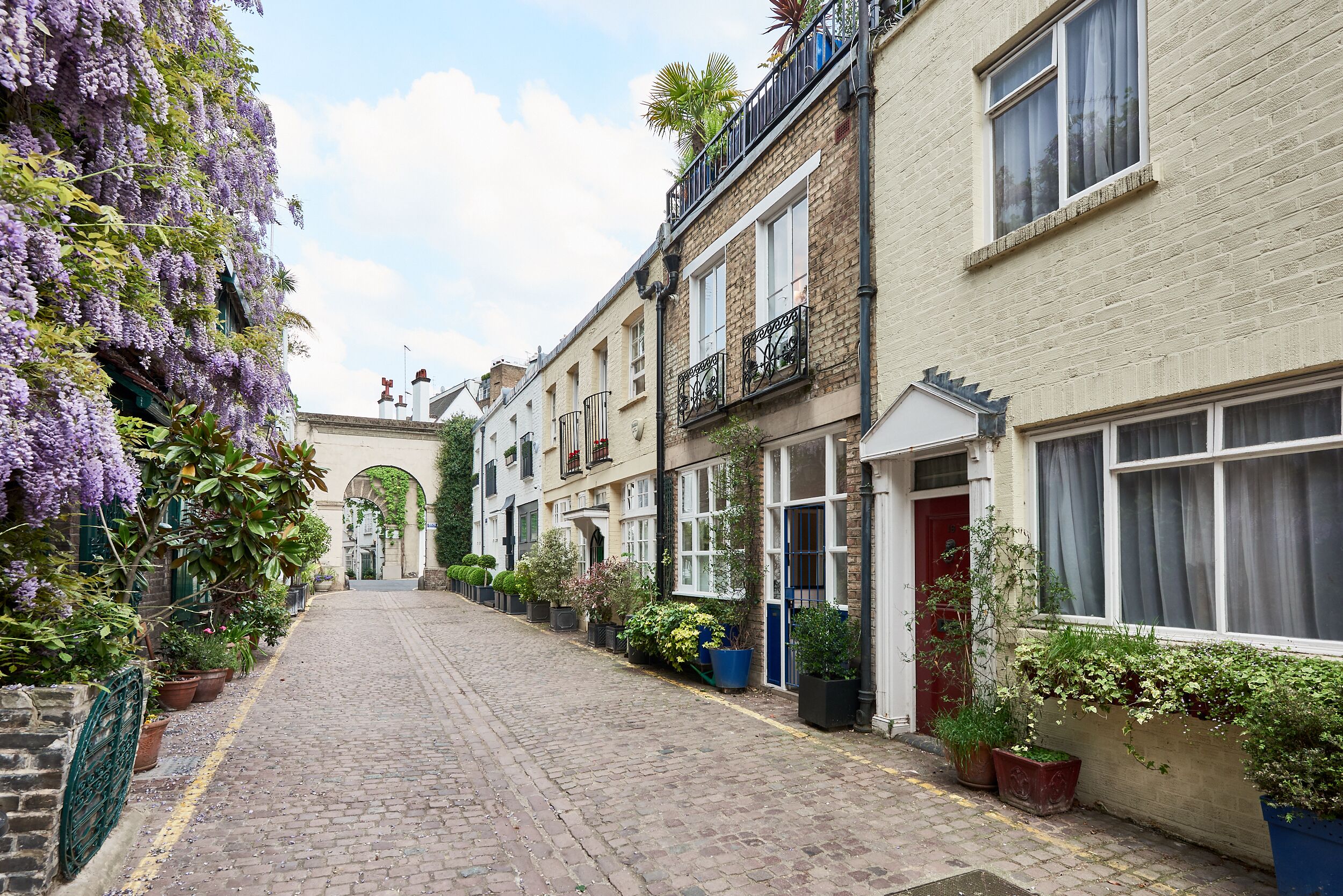 A narrow cobblestone street lined with terraced houses, each with a balcony and potted plants.