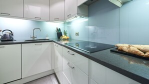 Una cocina moderna con armarios blancos, encimera negra y hervidor de acero inoxidable.