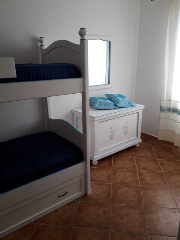 Una cama litera con una cama inferior, una mesita de noche con espejo y una ventana con cortinas.