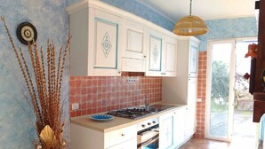 A kitchen with white cabinets, a gas stove, and a blue vase with dried plants. - The Lapwings (Calasetta)