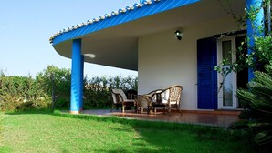 A covered outdoor seating area with wicker chairs, a blue door, and a white wall. - The Lapwings (Calasetta)