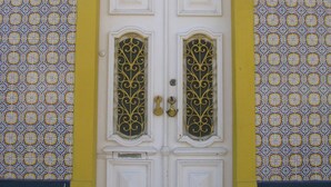 A double door with ornate metal grilles, a yellow arch, and a patterned wall.