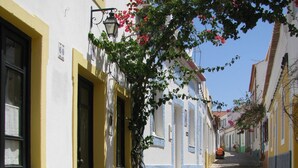 A narrow cobblestone street flanked by buildings with yellow and white facades, a clear blue sky, and a pedestrian in the distance.