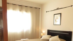 A hotel room with a bed, a nightstand, a lamp, and a window with curtains.