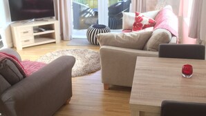 Een moderne woonkamer met een flatscreen-televisie, een bank, een eettafel en een schuifdeur die uitkomt op een buitengebied.