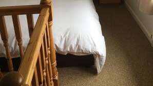 Een slaapkamer met een bed, een houten dressoir, een nachtkastje en een spiegel.