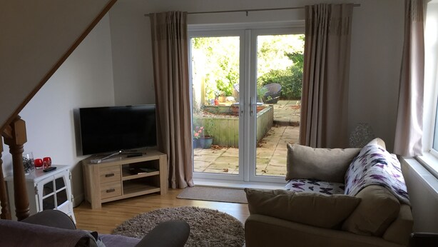Een woonkamer met een televisie op een houten standaard, een bank, een salontafel en een glazen schuifdeur die uitkomt op een tuin.
