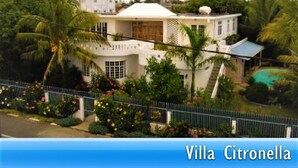 Villa Citronella, una casa blanca grande con varios niveles, rodeada de exuberante vegetación y una piscina.