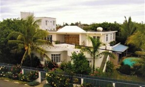 Villa Citronella, una casa blanca grande con varios niveles, rodeada de exuberante vegetación y una piscina.