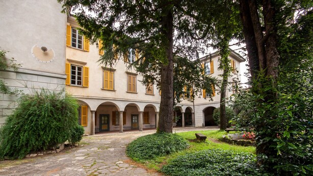 A courtyard with stone paving, arched walkways, and lush greenery.