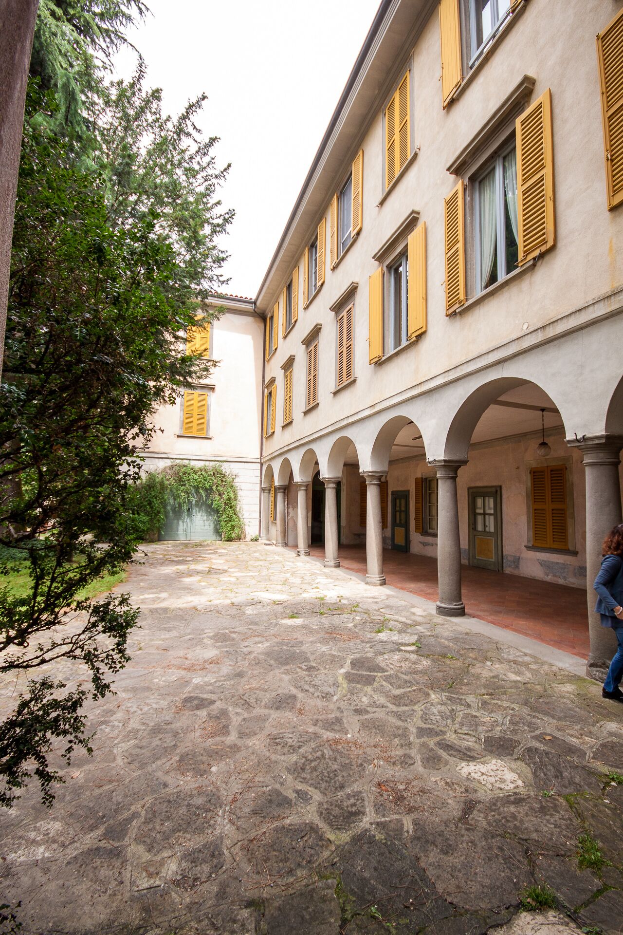 A courtyard with stone flooring and yellow shutters on the building.