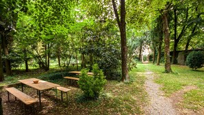 A serene outdoor dining area with wooden tables and benches, surrounded by lush greenery and trees.
