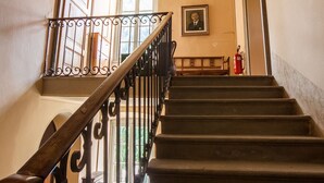 A staircase with a wooden handrail and black balusters, leading to a landing with a framed portrait and a fire extinguisher.