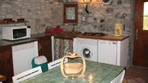 A compact kitchen with a stone wall, a microwave, a sink, a washing machine, and a table with a chair. - Rochecolombe: Apartment/ flat - ROCHECOLOMBE (Rochecolombe)