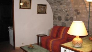 A cozy living room with a stone wall, a sofa, a table with a lamp, and two framed pictures on the wall. - Rochecolombe: Apartment/ flat - ROCHECOLOMBE (Rochecolombe)
