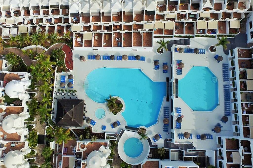 Vista aérea de un complejo turístico con varias piscinas, tumbonas y palmeras.